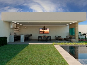A modern outdoor living space featuring a covered patio with a ceiling fan and integrated lighting. To the left, there is an outdoor kitchen equipped with a grill, countertops, and bar stools. The center has a dining table with chairs, and on the right is a lounge area with a sofa and coffee table. The patio overlooks a pool and lush green lawn. There are decorative plants and a blue sky with some clouds.