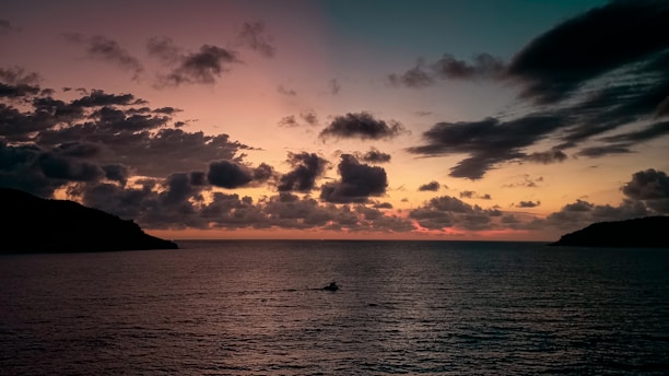A serene sunset view over the Andaman Islands' turquoise waters with a small boat in the distance.