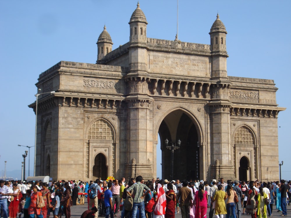 um grande grupo de pessoas fora de um grande edifício de pedra com Gateway of India ao fundo