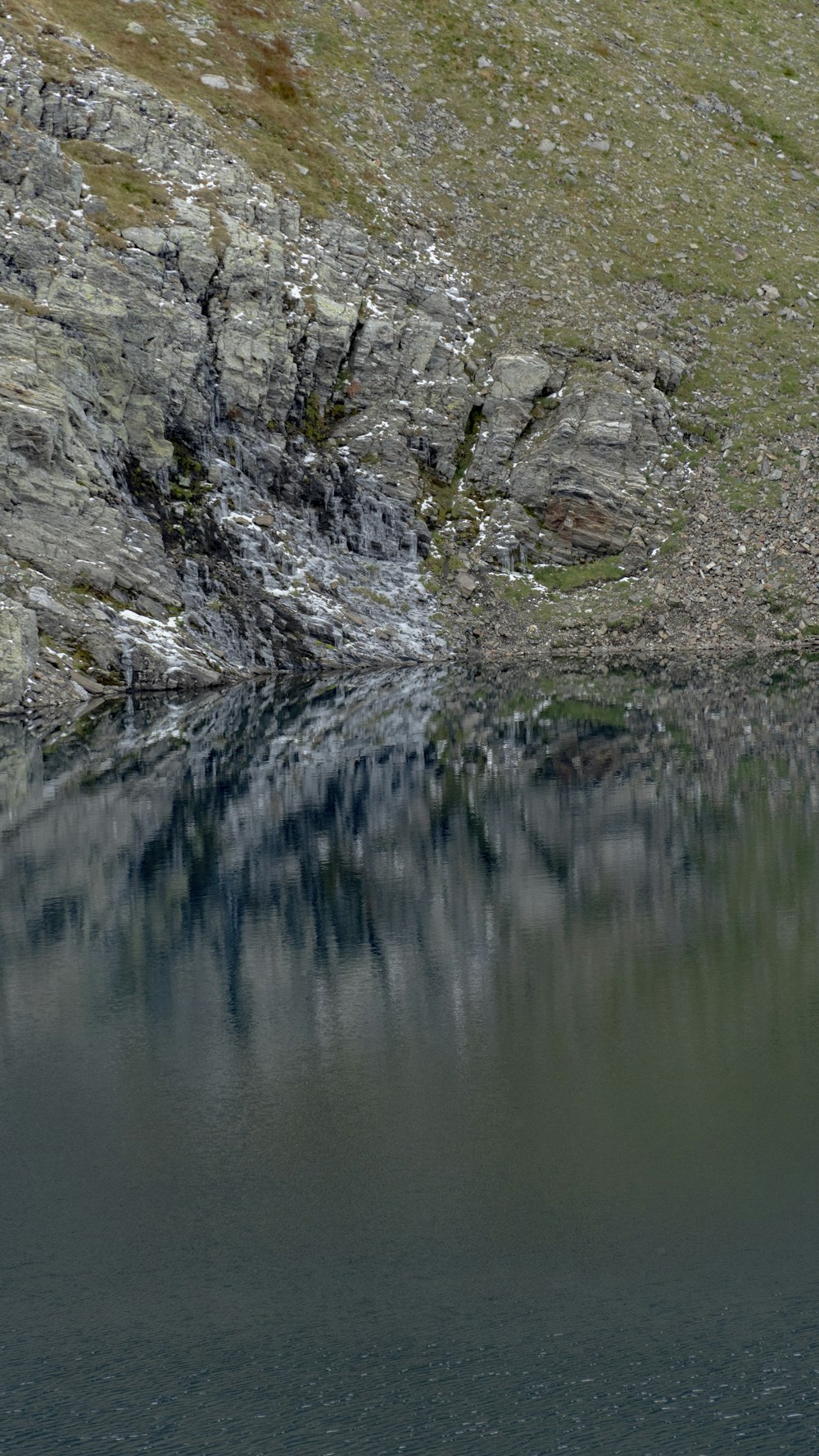 a body of water with a rocky cliff and plants on the side