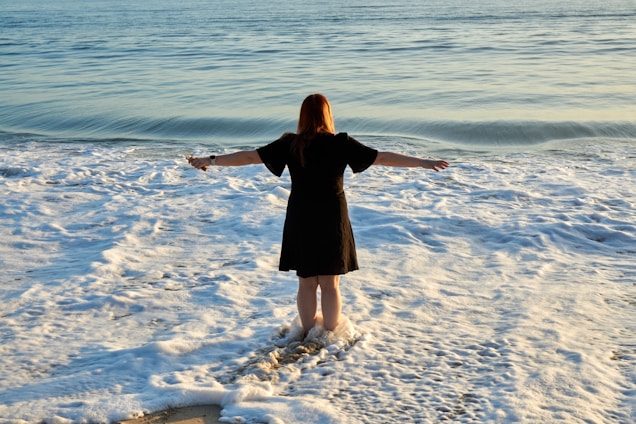 A woman standing at the shore, waves gently curling around her ankles at sunrise, embodying calm strength and connection with the sea.