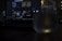 A dimly lit scene featuring a laptop with a music streaming service interface on the screen. Playlists and music recommendations are visible. A glass with water is positioned in front of the screen, capturing reflections and adding a subtle glow to the foreground.