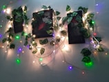 A wall is adorned with vine-like artificial green leaves intertwined with colorful string lights. The arrangement is centered around framed artworks featuring floral motifs, creating a lush, vibrant aesthetic.