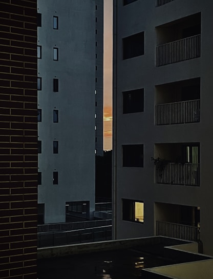 A sleek, modern apartment building with large windows overlooking a vibrant cityscape at sunset.