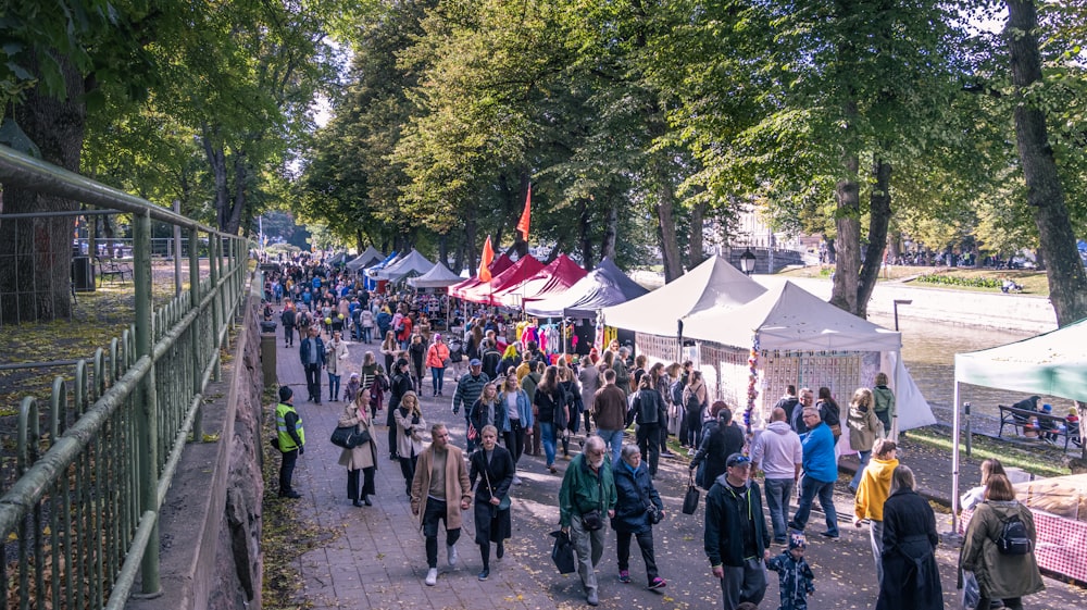 a crowd of people walking around a park with tents