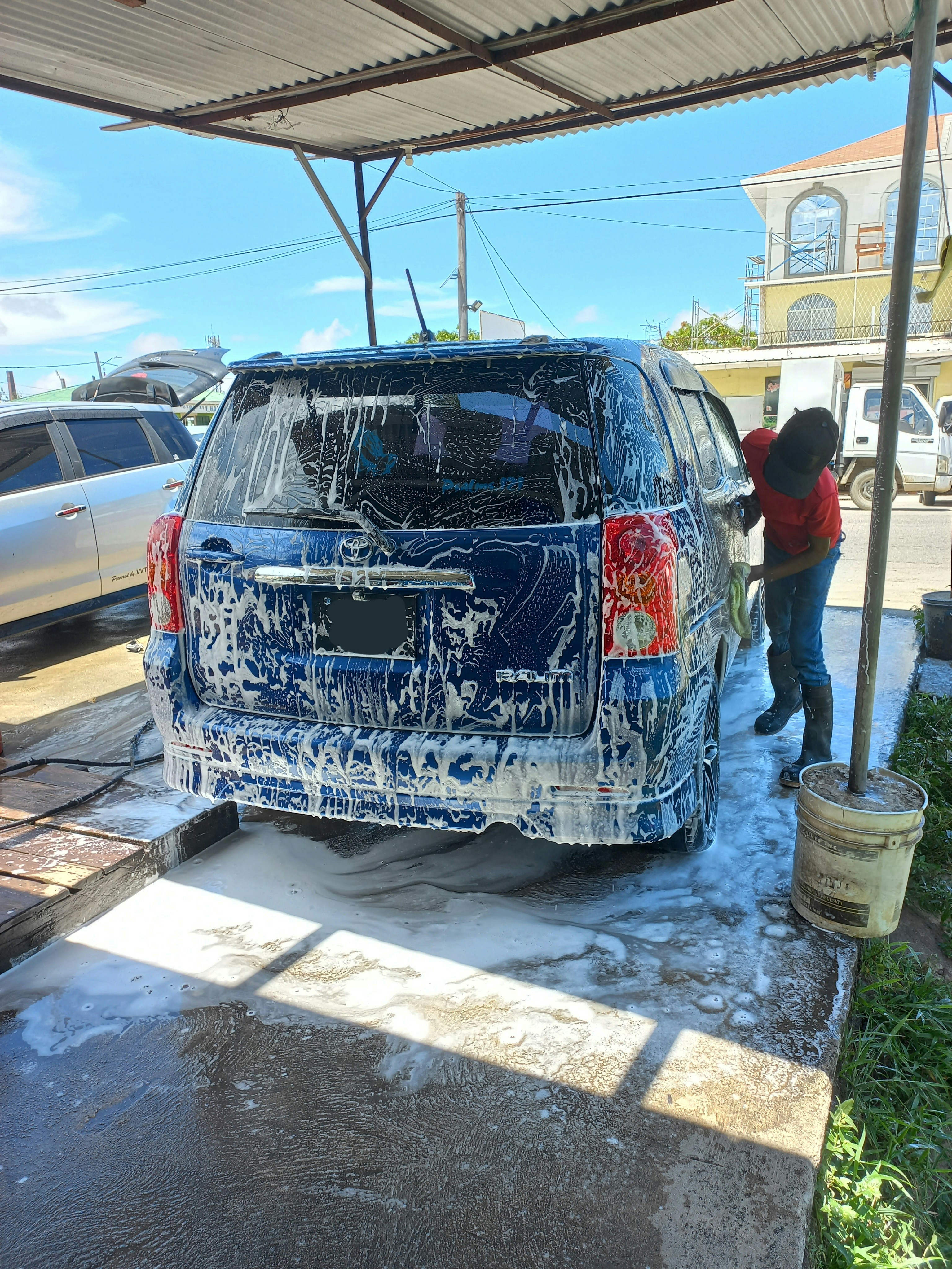Car exterior being hand-washed with soap suds, bright sunlight on gleaming paint
