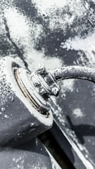 A weathered metal surface with visible rust and peeling paint, showcasing a close-up view of a bolt and pipe junction. The area appears corroded and worn, with textures of flaking paint and surface irregularities.