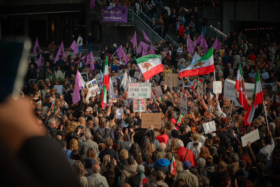 Crowd of protesters gathered, holding signs and banners, wearing red, white, and green clothing