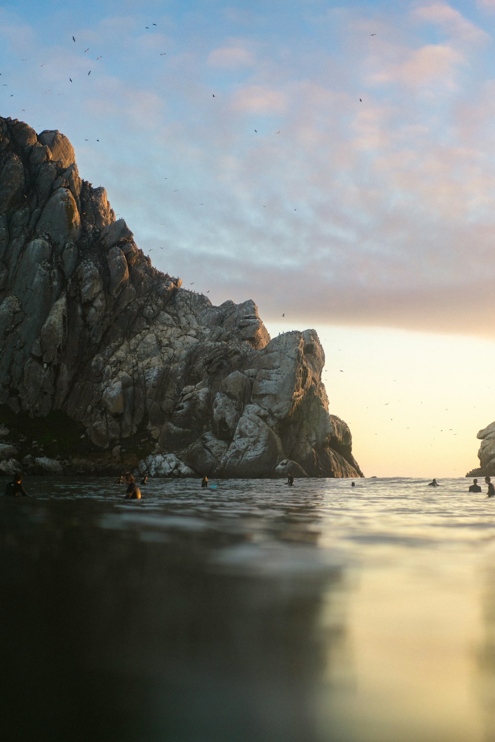 a body of water with a group of people in it and large rocks in the background