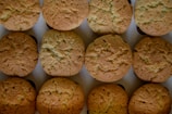A neat arrangement of freshly baked golden-brown cookies placed in three rows on a flat surface, each displaying a slightly cracked top indicating a crispy texture.