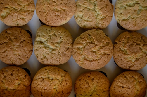 A neat arrangement of freshly baked golden-brown cookies placed in three rows on a flat surface, each displaying a slightly cracked top indicating a crispy texture.