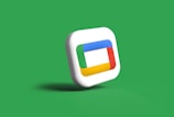 A three-dimensional rounded square icon with a layered, multicolored frame design is centered against a solid green background. The frame within the icon incorporates bright colors such as blue, red, yellow, and green, each section distinct in a continuous loop.