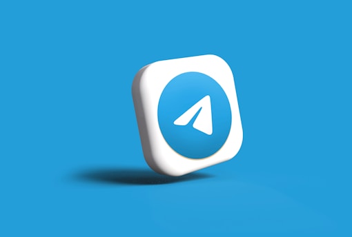 A three-dimensional, rounded square icon featuring a blue circle with a white paper airplane logo, set against a light blue background. The icon appears to be floating or slightly tilted.