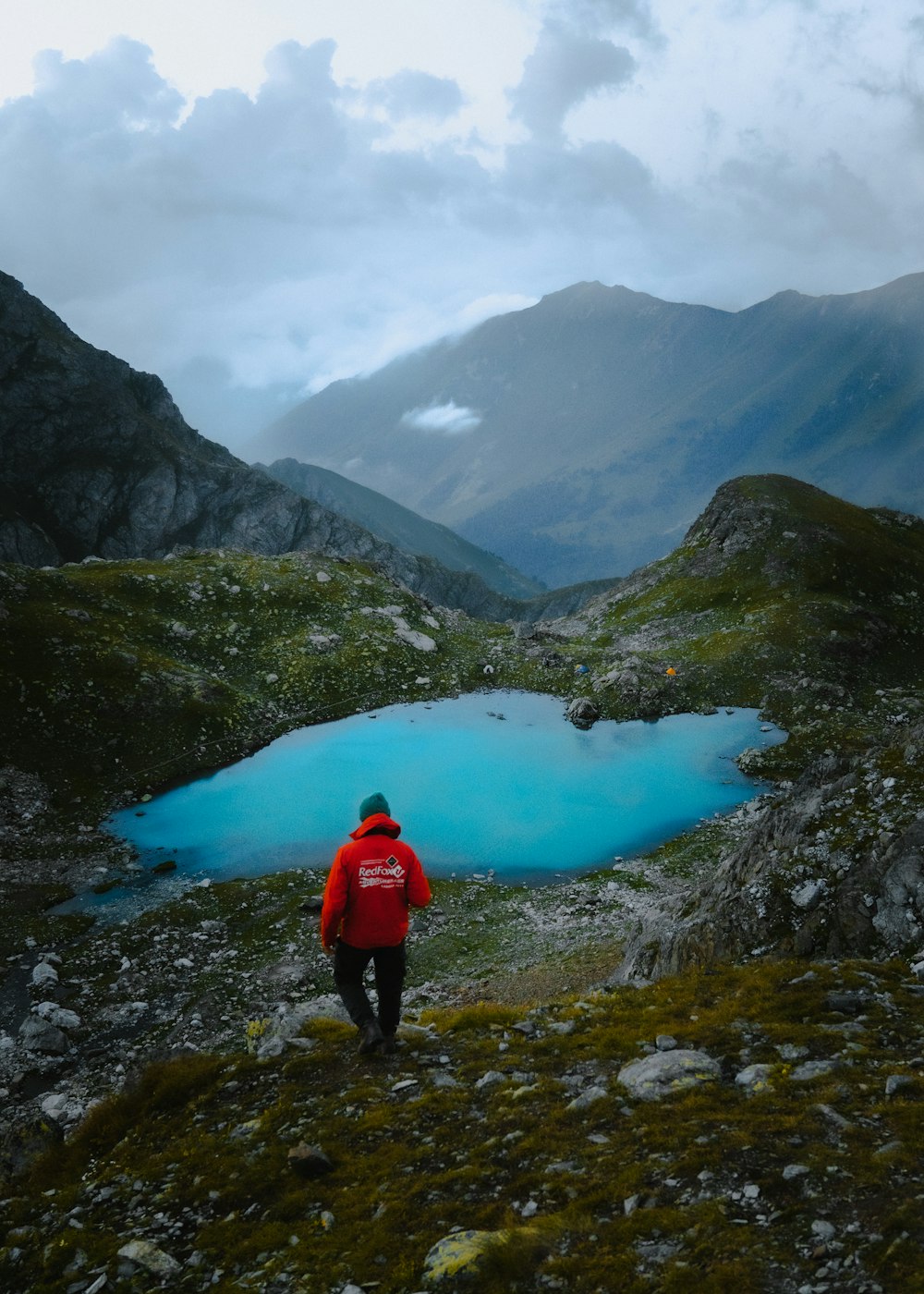 a person standing next to a body of water surrounded by mountains