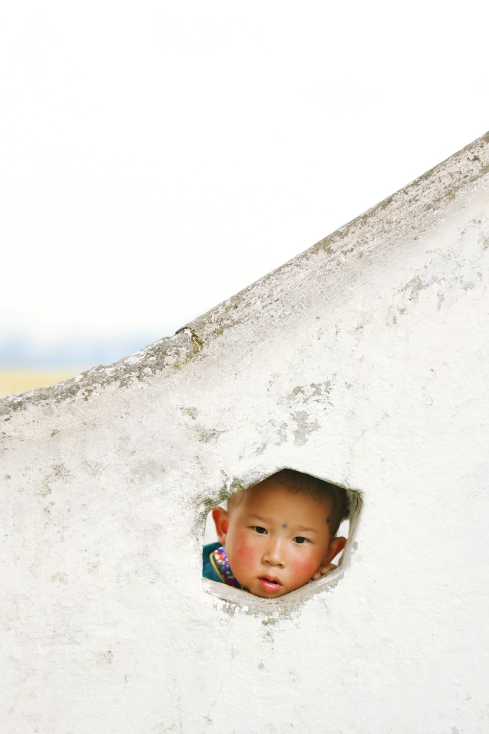 a boy peeking out of a hole in a rock