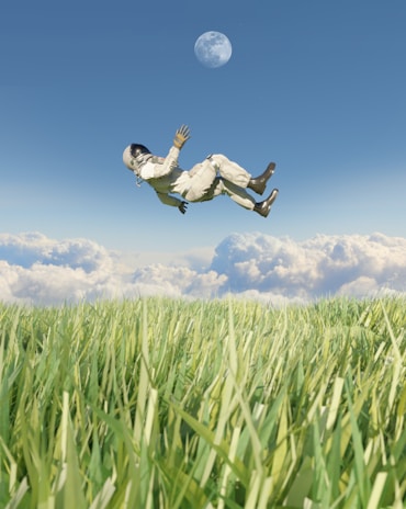 An astronaut in a white spacesuit is floating above a lush green field with long grass. Fluffy white clouds gather near the horizon under a clear blue sky. The moon is visible in the sky, adding a surreal element to the scene.