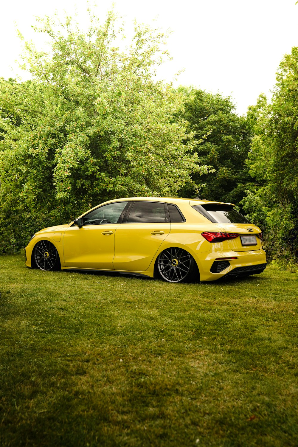 a yellow car parked in a grassy area with trees in the background