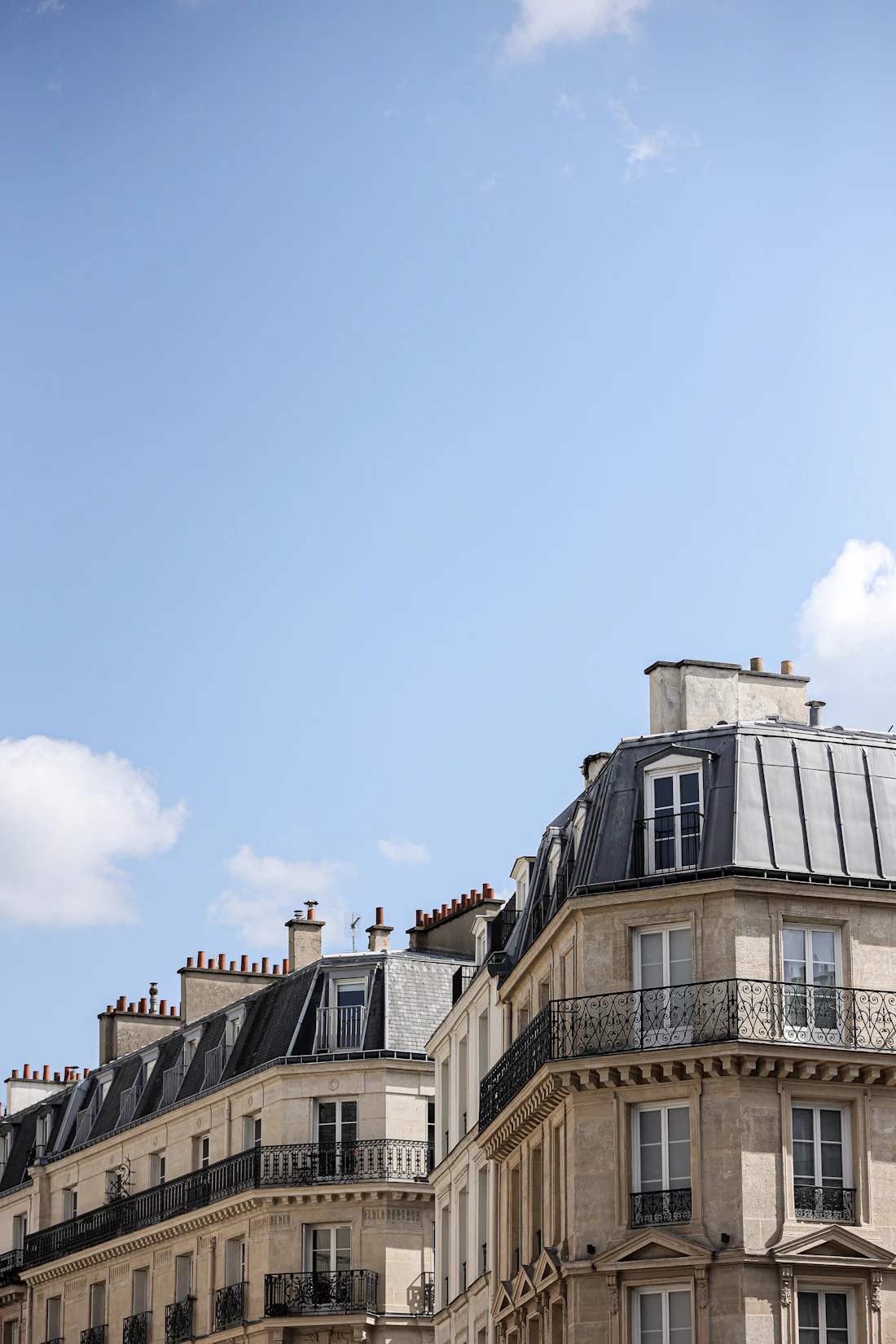 Toiture en zinc d'un immeuble parisien, lucarnes et cheminées sous un ciel bleu
