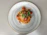 A plate of spaghetti topped with tomato sauce, cherry tomatoes, grated cheese, and fresh basil garnish is placed on a simple, light gray plate against a neutral colored background.