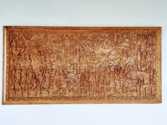 An intricately carved wooden panel depicting a detailed scene featuring numerous figures and animals. The panel has a variety of characters engaged in activities, surrounded by dense foliage and mythical creatures. The craftsmanship showcases elaborate patterns and textures throughout the artwork.