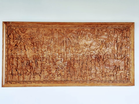 An intricately carved wooden panel depicting a detailed scene featuring numerous figures and animals. The panel has a variety of characters engaged in activities, surrounded by dense foliage and mythical creatures. The craftsmanship showcases elaborate patterns and textures throughout the artwork.