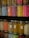Colorful jars filled with a variety of small decorative sprinkles, including pearls and rods, arranged tightly on shelves. The jars are transparent, allowing the vibrant colors of the contents to stand out against the darker background.