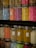 Colorful jars filled with a variety of small decorative sprinkles, including pearls and rods, arranged tightly on shelves. The jars are transparent, allowing the vibrant colors of the contents to stand out against the darker background.