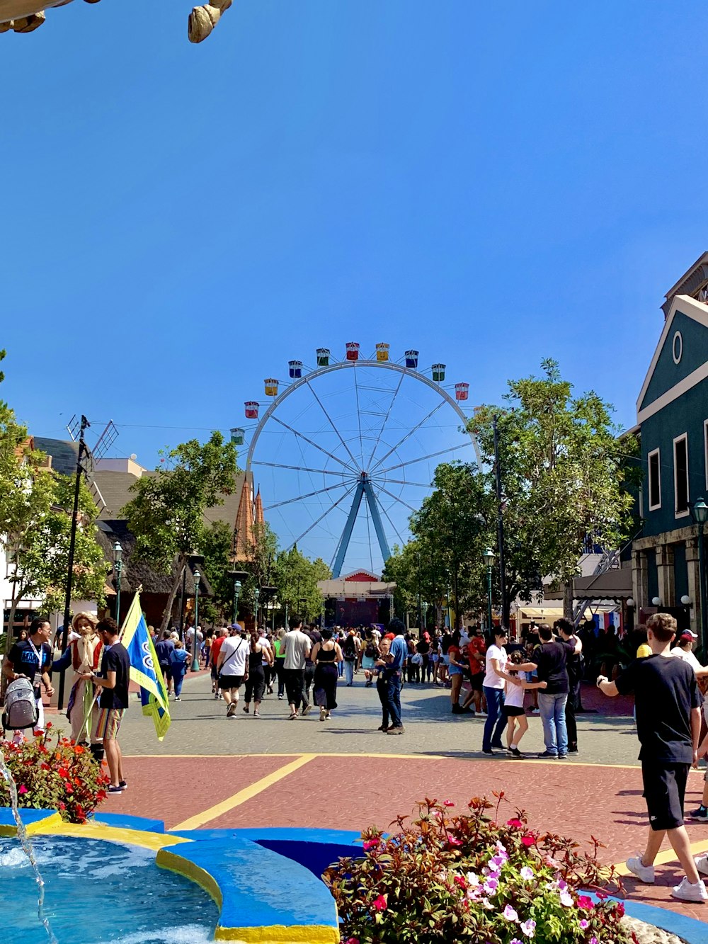 Una folla di persone che camminano intorno a una grande ruota panoramica