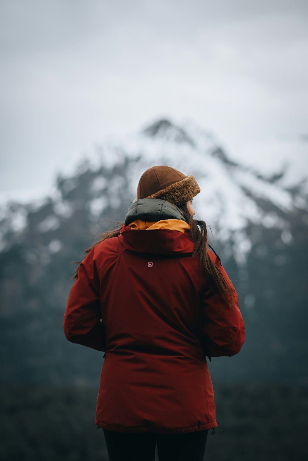 a person wearing a red jacket and a hat with a mountain in the background