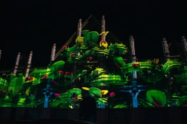 A building facade is illuminated with a vibrant projection of green cacti with pink flowers. The design integrates with the architectural features, using light to create a lively and artistic display.