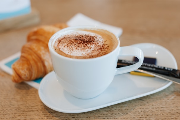 A steaming cup of espresso next to a chocolate croissant on a cozy café counter