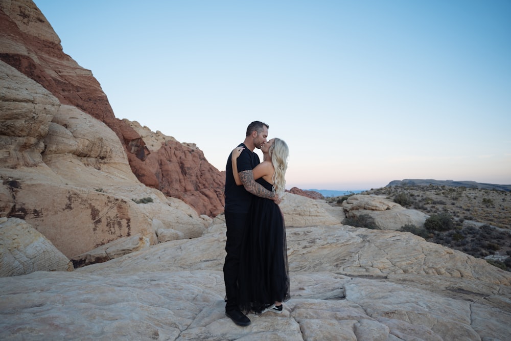 a man and woman kissing on a rocky beach