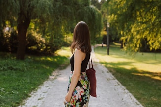 A woman carrying a casual handbag while walking in a park.