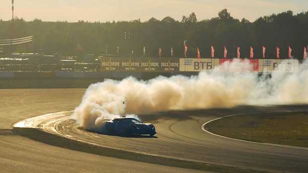 A close-up shot of a drifting car kicking up smoke on a Baltic racetrack during sunset.