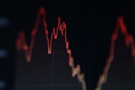 A red line graph with peaks and valleys on a dark background, indicating fluctuations in data or statistics.