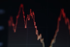A red line graph with peaks and valleys on a dark background, indicating fluctuations in data or statistics.