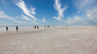 A group of travelers walking across the endless white salt flats under a vibrant sunset sky.