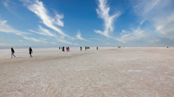 A group of travelers walking across the endless white salt flats under a vibrant sunset sky.
