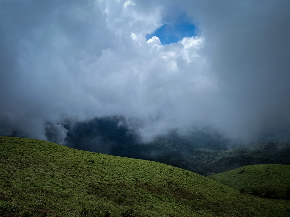 a grassy hill with clouds above