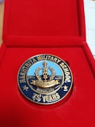 A commemorative medal celebrating the 75th anniversary of Rashtriya Military School, neatly placed inside a red presentation box. The medal features detailed engravings and inscriptions, showcasing a laurel wreath and the years '1946 - 2021'. The words 'Bengaluru' and '75 Years' are prominently displayed.
