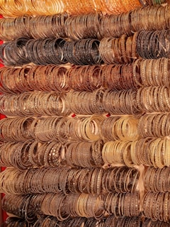 Multiple rows of intricately designed bangles are displayed, exhibiting a variety of metallic tones. The collection is arranged systematically, showcasing a gradient from gold to bronze and brown, with each piece featuring detailed patterns and embellishments.