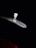 A small, transparent vial with a white cap is placed on a metallic surface against a dark background. The lighting highlights the vial and part of the metallic surface, creating a focused and dramatic contrast.