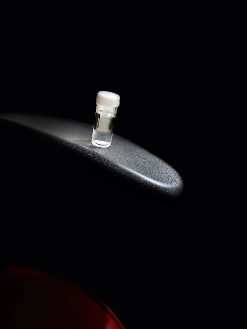 Close-up of a sleek black lab vial with gold accents, resting on a reflective surface.