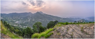 A panoramic view of rolling hills and valleys covered in rich green foliage at sunset.