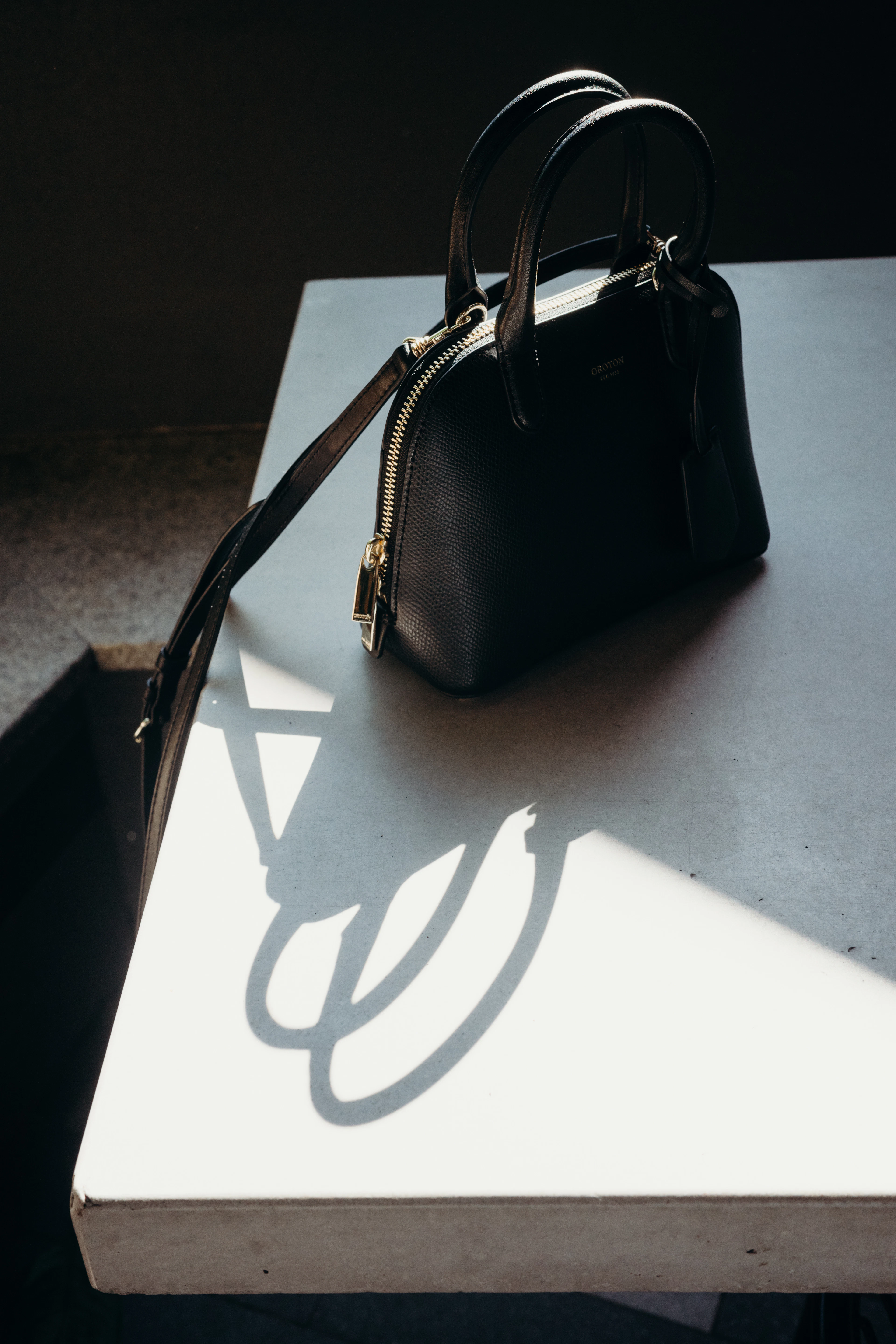 Black leather top-handle bag on a white plinth in raking sunlight