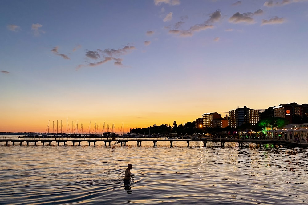 a person standing in a body of water with a bridge and buildings in the background