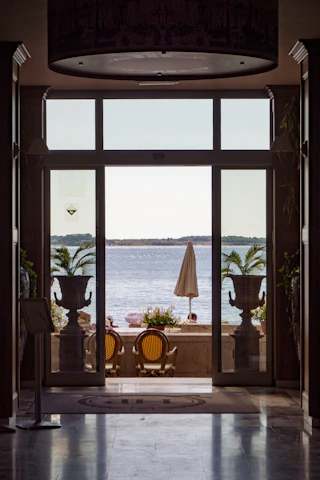 a patio with a table and chairs and a large window with a view of the ocean