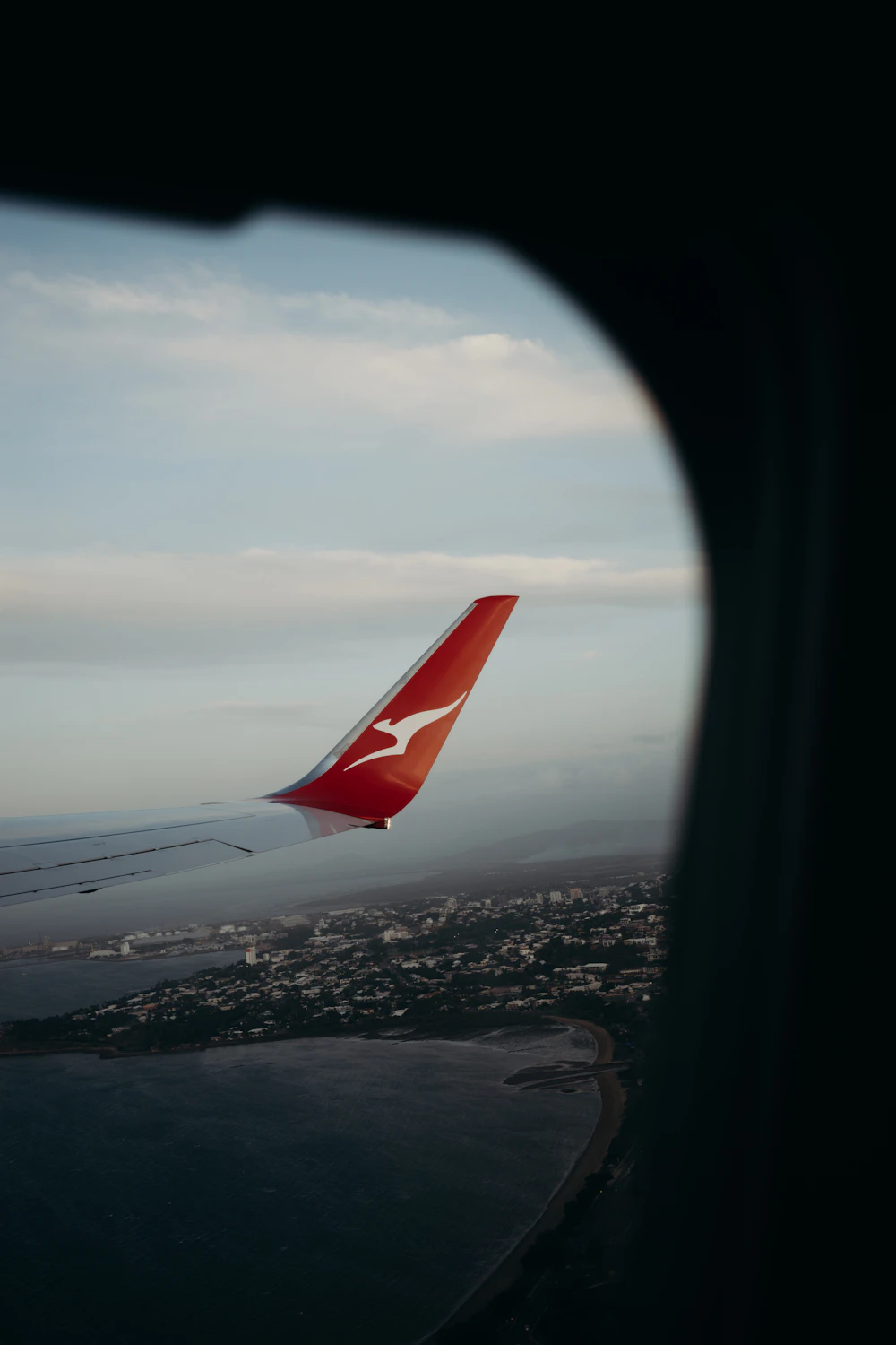 An aircraft wing tip seen through the window above a coastal town