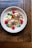 A white bowl filled with granola, raspberries, blueberries, coconut flakes, and garnished with fresh mint leaves, placed on a rustic wooden table.