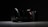 A high-quality camera with a large lens is set against a dark background. The camera is positioned at an angle, with the lens prominently in focus. The overall lighting is low, highlighting the camera's sleek design and details on the lens and body.